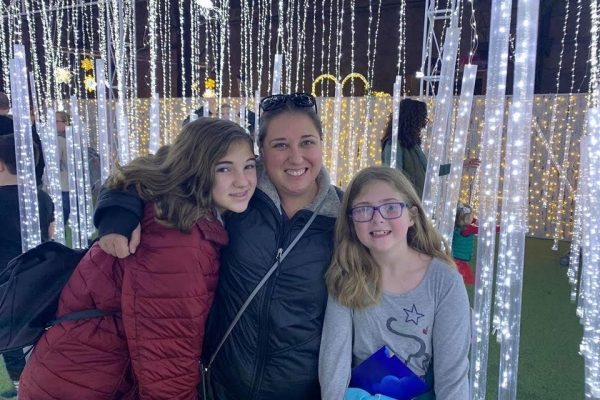 A White mother and her two young daughters in front of a curtain of sparkling lights
