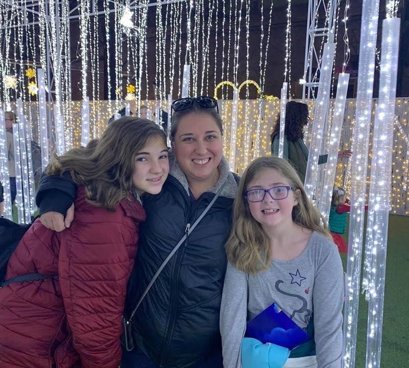 A White mother and her two young daughters in front of a curtain of sparkling lights