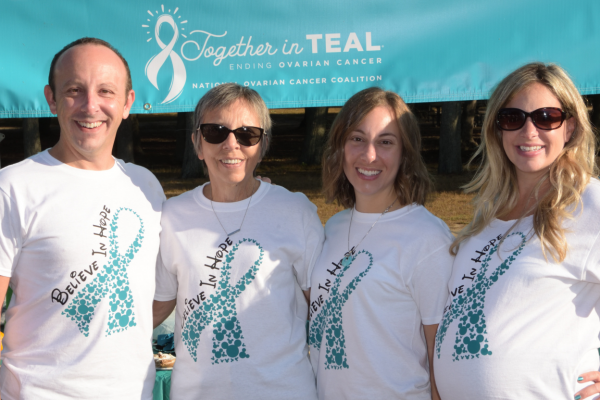 Three adult females and a male standing under a Together in Teal banner