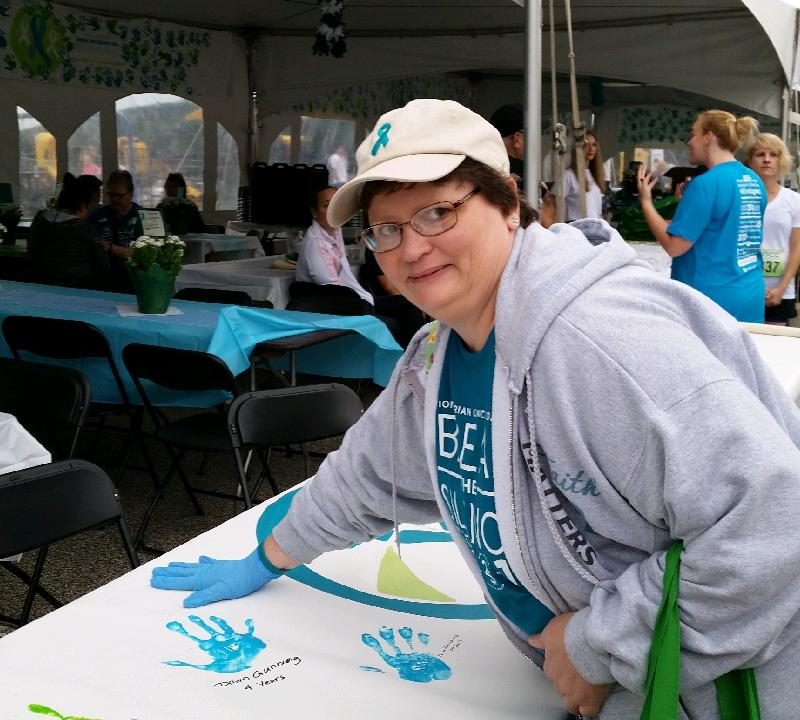 A survivor in a baseball cap with a teal ribbon logo leaves a teal handprint on a poster