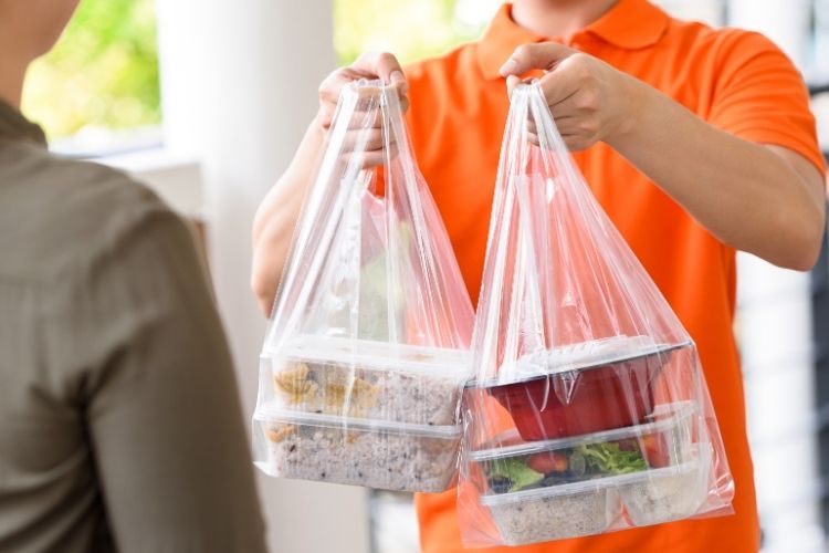 a person in an orange shirt is holding two plastic bags with food in them